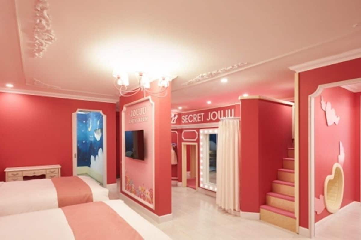 Una habitación en tonos rosados, con una cama, un tocador y una escalera.