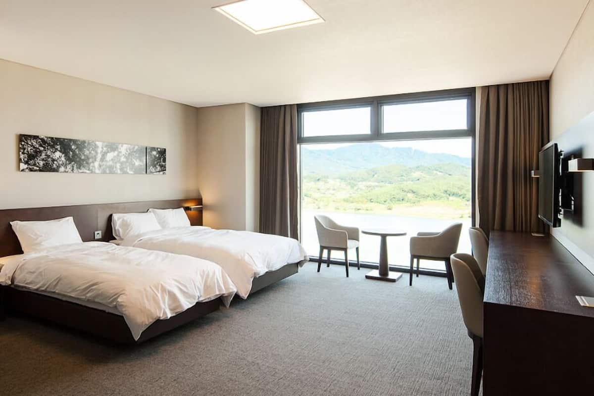 Habitación de hotel con una cama grande, un escritorio con silla, televisor y ventana con vista a la montaña.