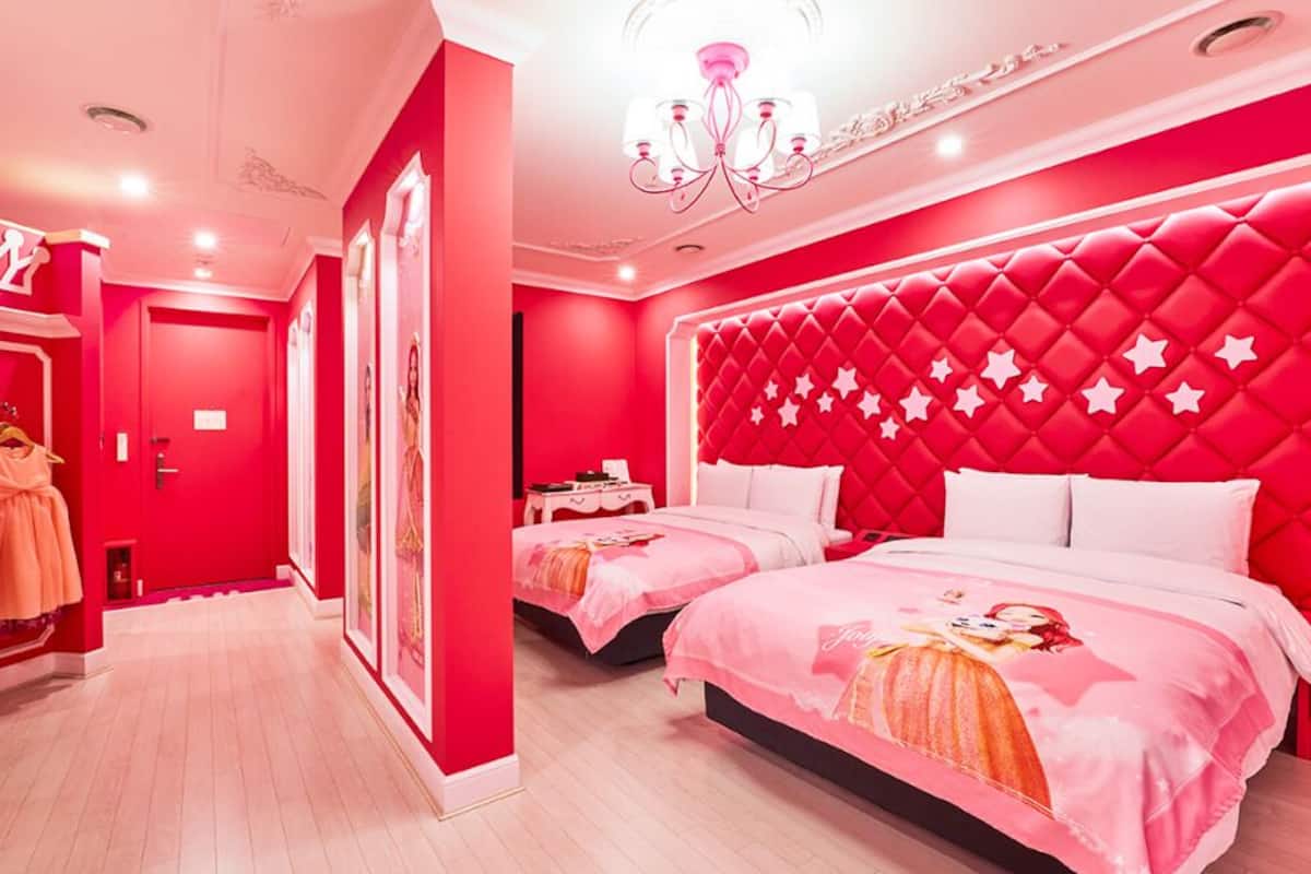 Una habitación con dos camas, una araña y una pared roja con motivos de estrellas.