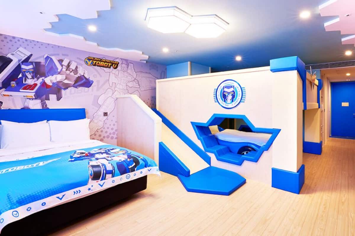 Una sala de juegos infantil con una cama, espacio para jugar y una pared con un mapa y un personaje de robot.