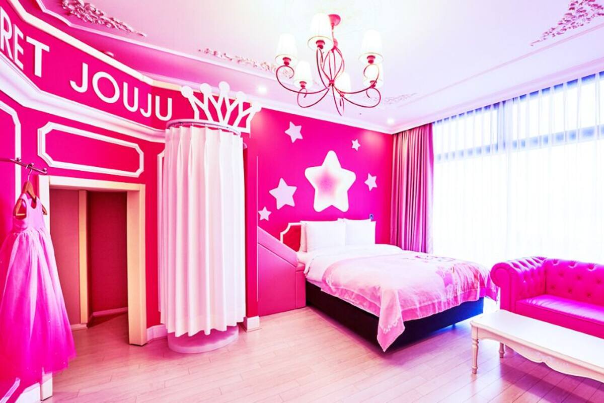 Una habitación de colores vivos con una cama, un sofá rosa y una araña.