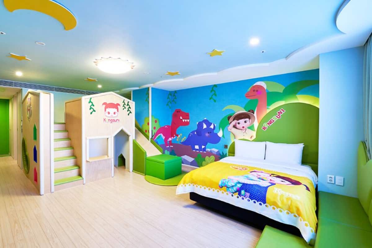 Una habitación infantil con cama, paredes verdes, zona de juegos y un mural.