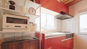 A modern kitchen with a microwave, stove, and red cabinetry. - V.Close to Shinjuku Kabukicho H (Shinjuku-ku)