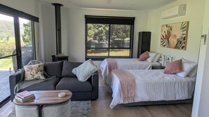 A modern room with a sofa, two beds, a small table, and a large window offering a view of the outdoors.