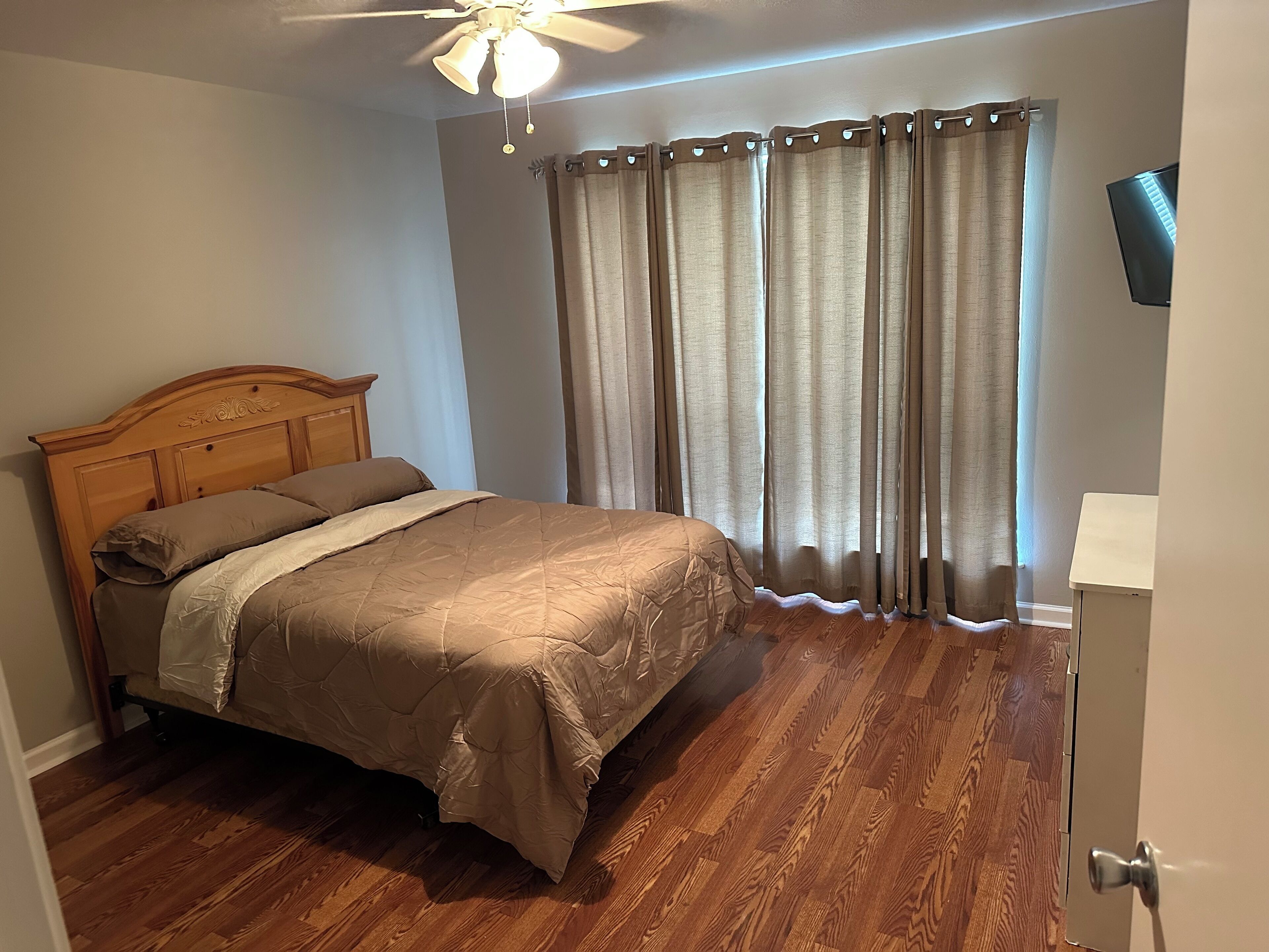 A bedroom with a wooden bed, a ceiling fan, and a TV on the wall.