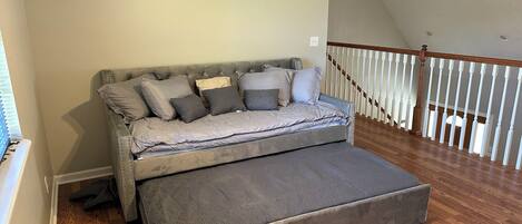 A bedroom with a bed, a wooden floor, a staircase, and a white railing.