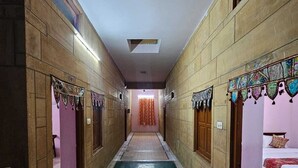 A corridor with a central green carpet, flanked by rooms with wooden doors and patterned curtains. - Hotel Blue Diamond Jaisalmer (Jaisalmer)