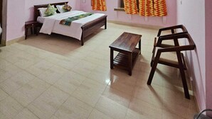 A bedroom with a bed, a small table, a chair, a ceiling fan, and curtains. - Hotel Blue Diamond Jaisalmer (Jaisalmer)
