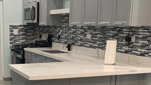 A modern kitchen with grey cabinets, a white countertop, and a black and white backsplash. - Charming 2-bedroom apartment with AC, WiFi in wonderful Nassau (Nassau)