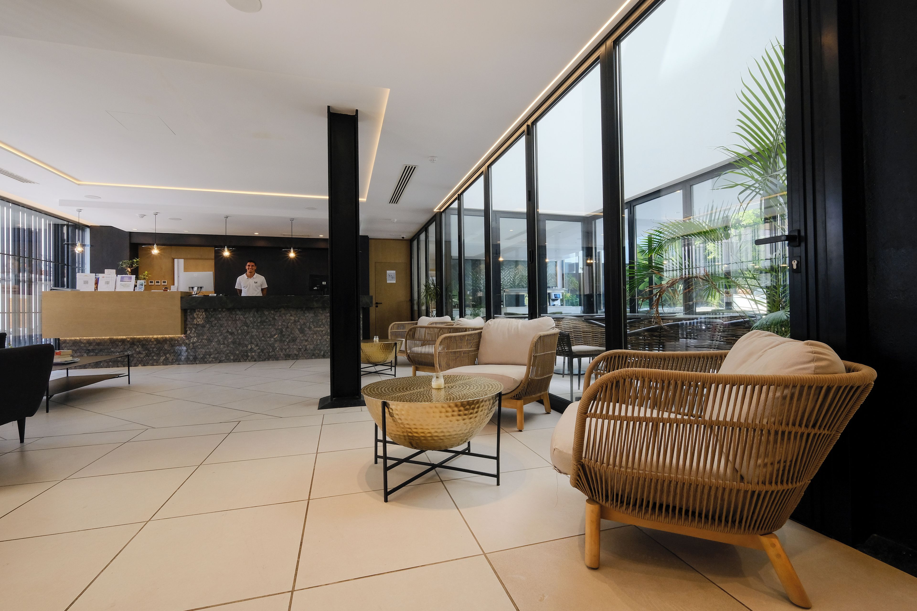 Um lobby moderno com balcão de recepção, área de estar e amplas janelas com vista para o exterior.