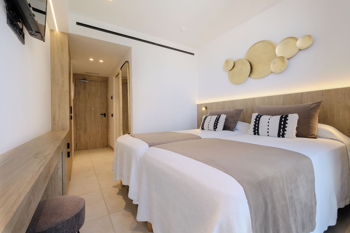 A modern bedroom with a large bed, two bedside tables, and a wall-mounted decorative piece.
