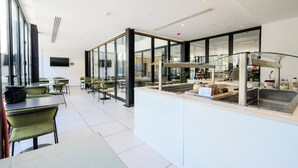 Ein modernes Restaurant mit Glastrennwänden, grünen Stühlen und einer zentralen Theke mit Spüle.