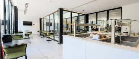 A modern restaurant with glass partitions, green chairs, and a central counter with a sink.