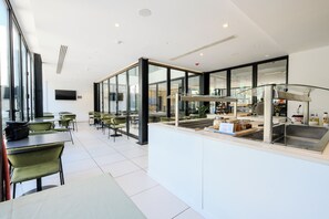 Um restaurante moderno com divisórias de vidro, cadeiras verdes e um balcão central com pia.