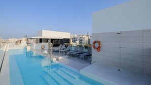 Una piscina en la azotea con sillones de descanso y un flotador en la pared.