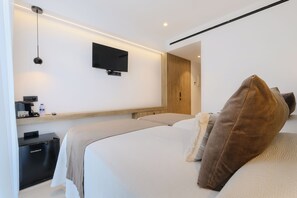 Une chambre d’hôtel moderne équipée d’un lit, d’un téléviseur à écran plat fixé au mur, d’un petit bureau avec une machine à café et d’un réfrigérateur compact.