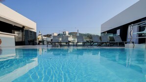 Ein Dachpool mit Liegestühlen und einem Tisch, umgeben von modernen Gebäuden und einem klaren Himmel.