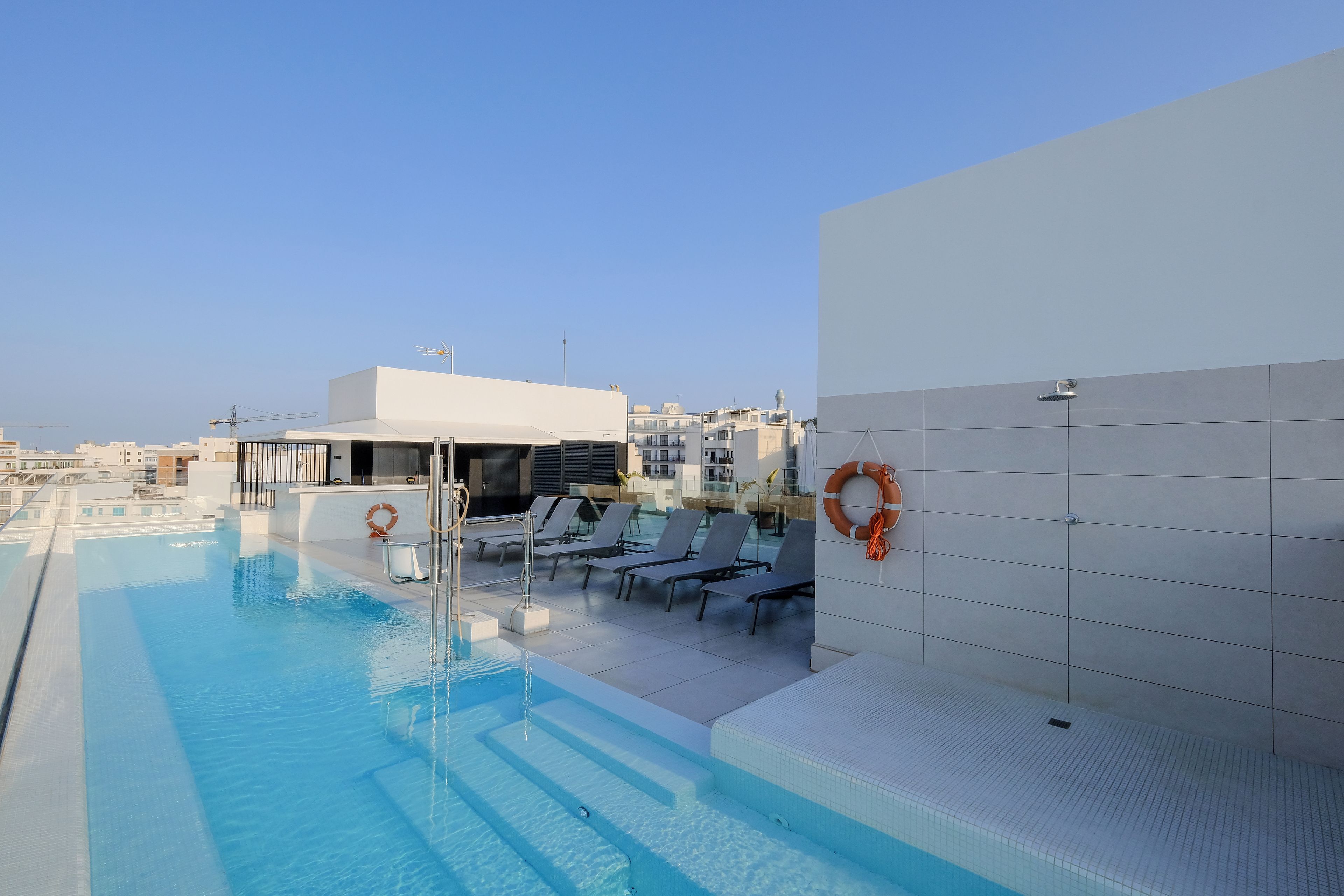 A rooftop pool with lounge chairs and a lifebuoy on the wall.
