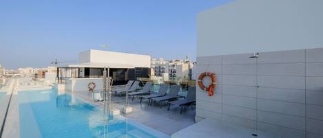 A rooftop pool with lounge chairs and a lifebuoy on the wall.