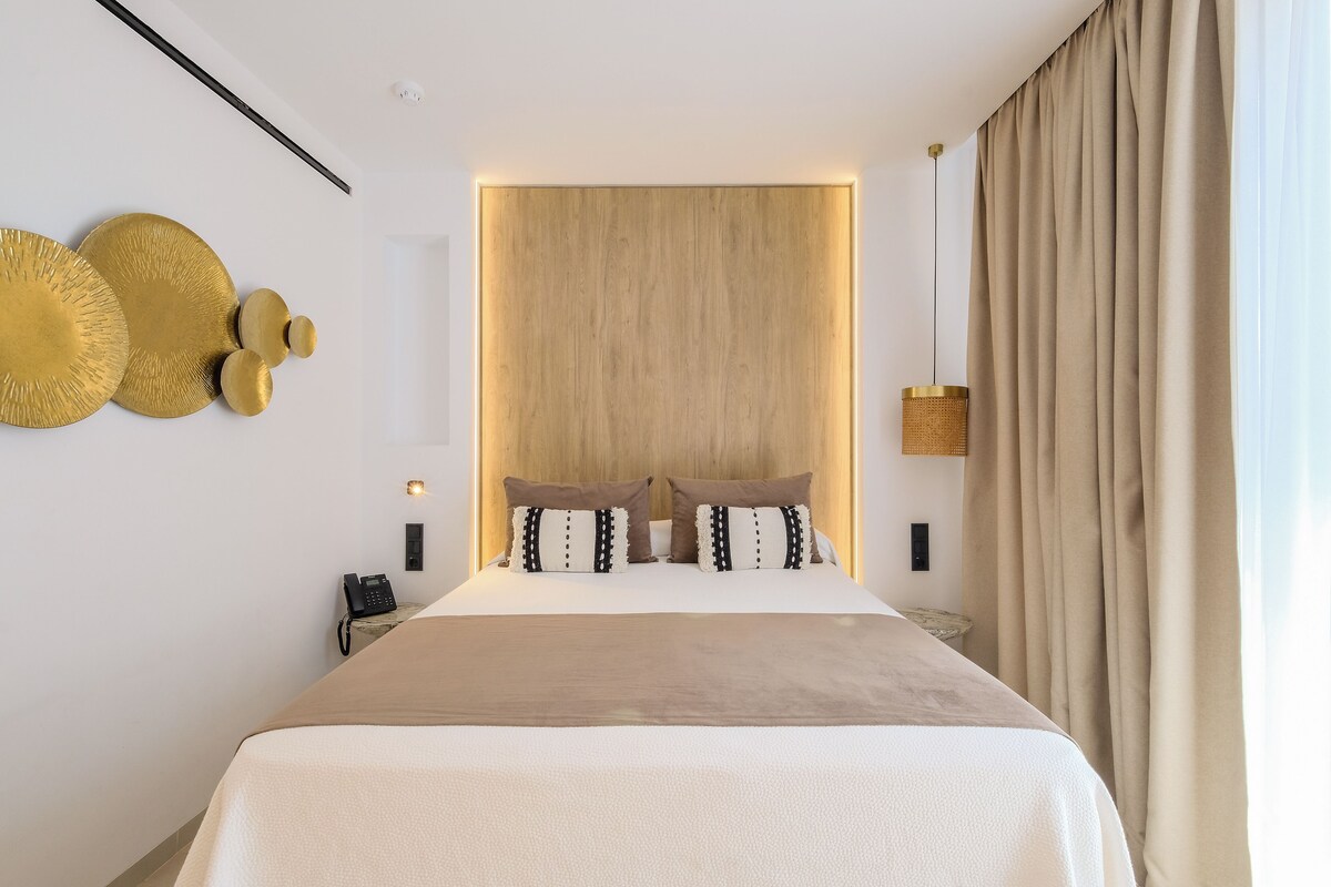 A modern bedroom with a large bed, a wooden headboard, and a bedside table with a lamp.