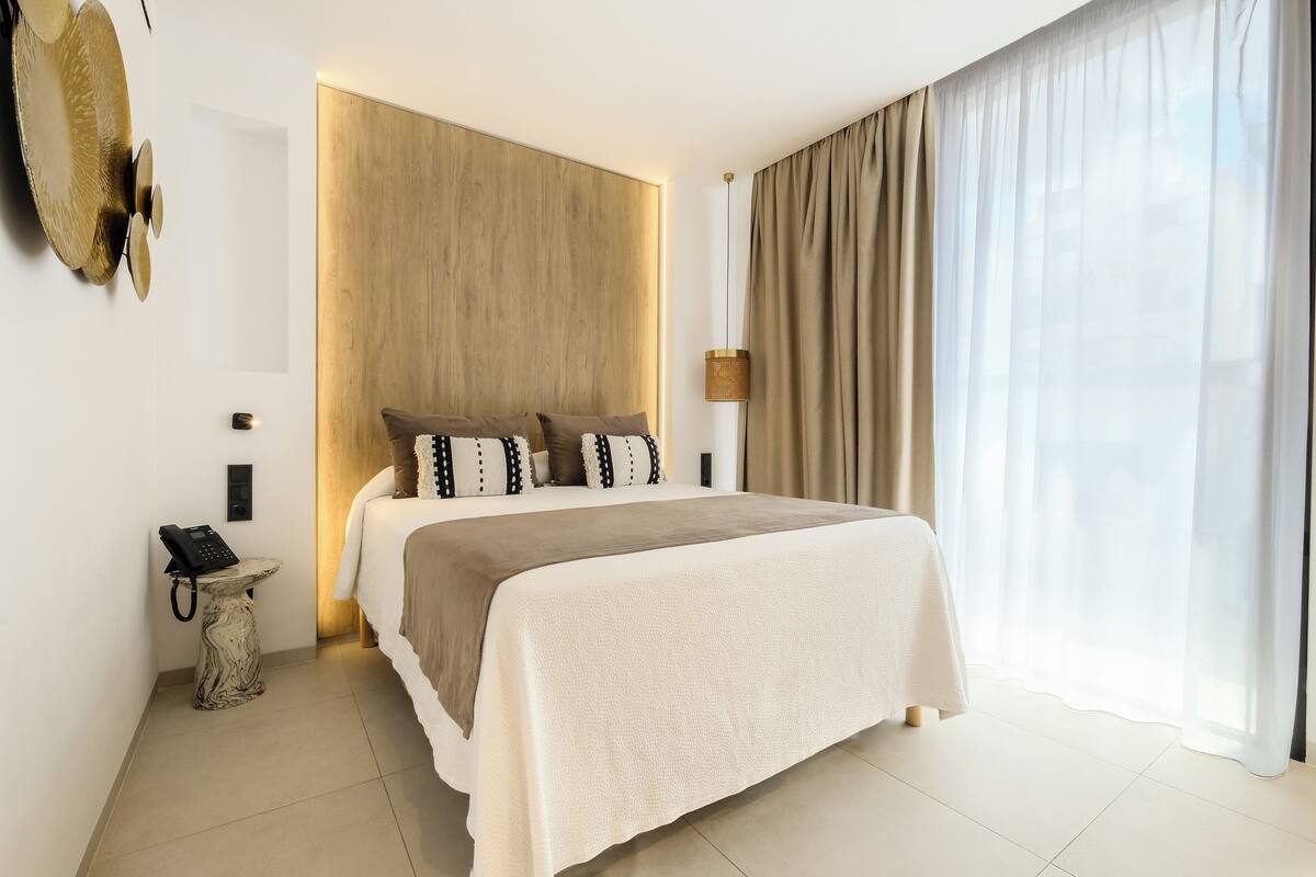 Habitación de hotel moderna con una cama grande, teléfono en la mesita de noche, lámpara y vistas al exterior.