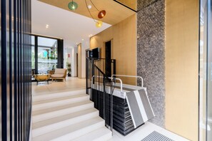 L’intérieur moderne d’un hôtel, avec un escalier, un téléviseur à écran plat fixé au mur et un coin salon comprenant un fauteuil en osier et un canapé.