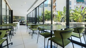 Un comedor moderno e interior con sillas y mesas verdes, ventanas amplias y vistas a un balcón con plantas.