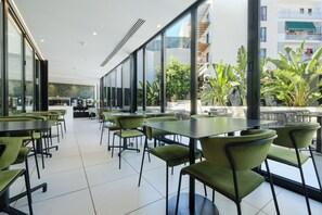 Ein moderner Essbereich mit grünen Stühlen und Tischen, großen Fenstern und Blick auf einen Balkon mit Pflanzen.