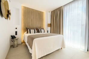 Ein modernes Hotelzimmer mit einem großen Bett, einem Nachttischtelefon, einer Lampe und Blick ins Freie.