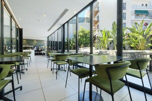 Un comedor moderno e interior con sillas y mesas verdes, ventanas amplias y vistas a un balcón con plantas.