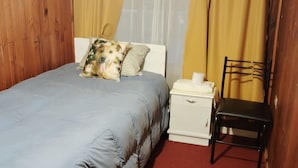 Une chambre à coucher avec un lit, une table de chevet, une chaise et une fenêtre avec des rideaux.