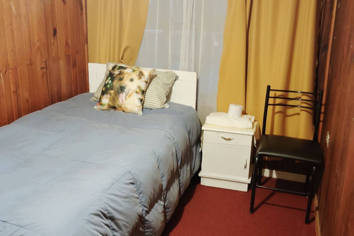 A bedroom with a bed, a nightstand, a chair, and a window with curtains.