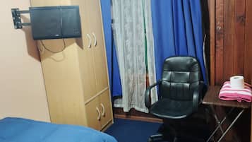 Um quarto pequeno com uma cama, uma escrivaninha, uma cadeira e um guarda-roupa.
