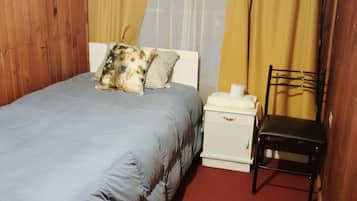 Quarto com cama, mesa de cabeceira, cadeira e janela com cortinas.