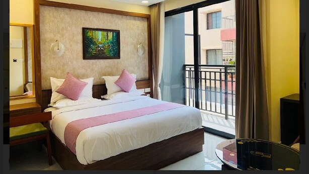 Une chambre d’hôtel avec un grand lit, un ventilateur de plafond, un tableau au mur et une vue sur le balcon extérieur.
