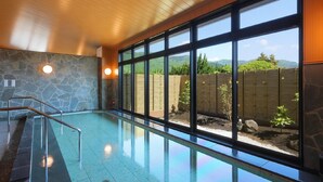 A swimming pool with a stone wall and large windows offering a view of a bamboo fence and greenery. - Aso Hakuunsansou (Aso)