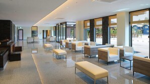 A spacious lobby with a long bench seating area, a reception desk, and large windows offering a view of the outside. - Aso Hakuunsansou (Aso)