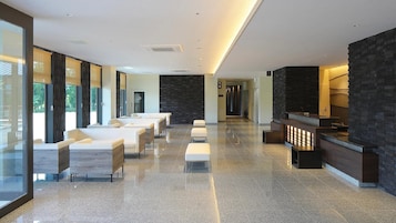 A modern hotel lobby with a long reception desk, seating area with sofas and chairs, and a stone accent wall.