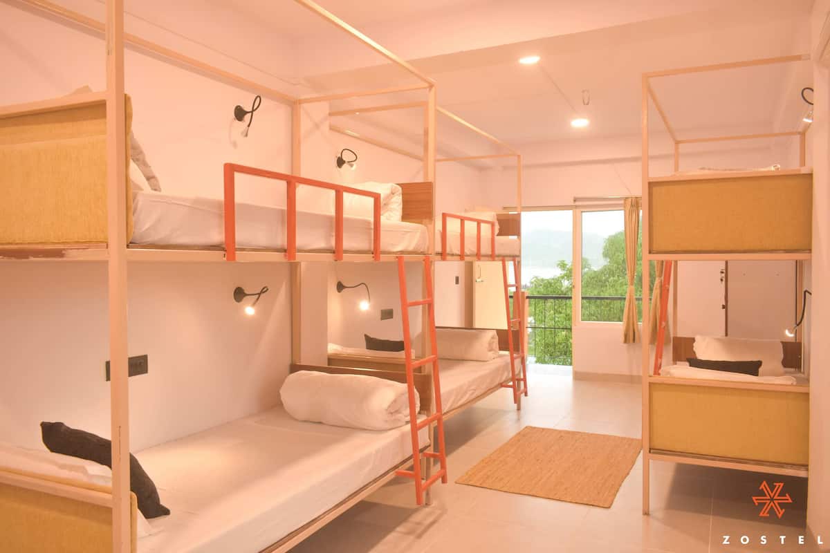Une chambre de type dortoir, avec des lits superposés, un petit bureau et une fenêtre donnant sur un espace verdoyant.