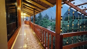 A corridor with patterned flooring, wooden railings, and a view of a mountainous landscape. - Lodging in Ollantaytambo living inka city with viewpoint to mountains (Ollantaytambo)