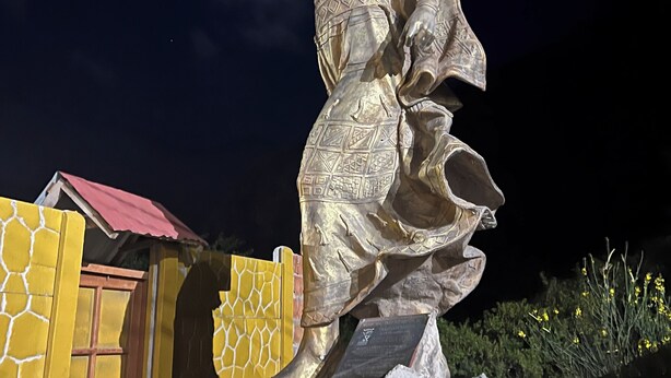 Une statue d’une femme vêtue d’une longue robe flottante, posée sur un socle rocheux.