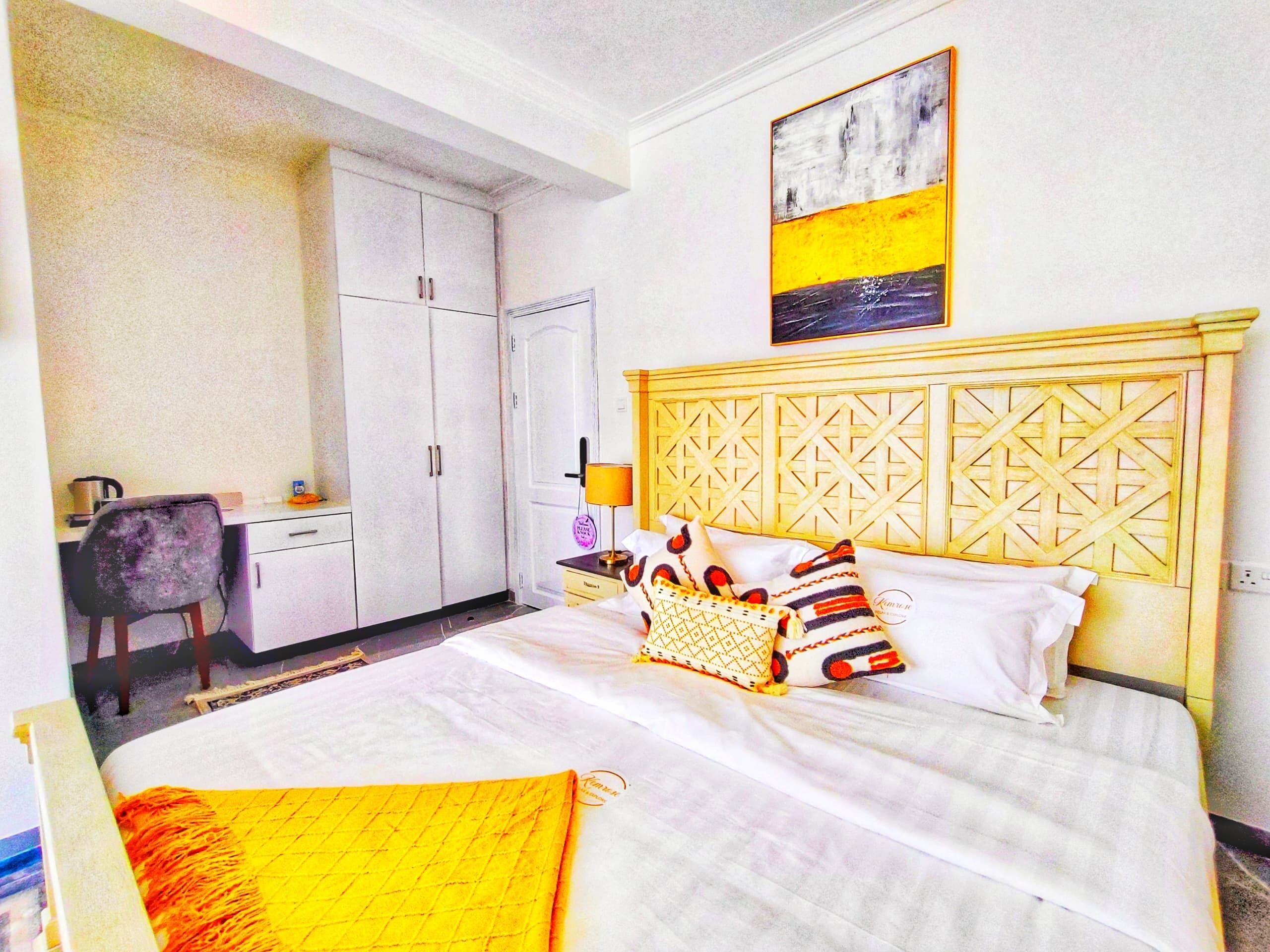 Habitación de hotel con cama, escritorio, silla, armario y un cuadro en la pared.