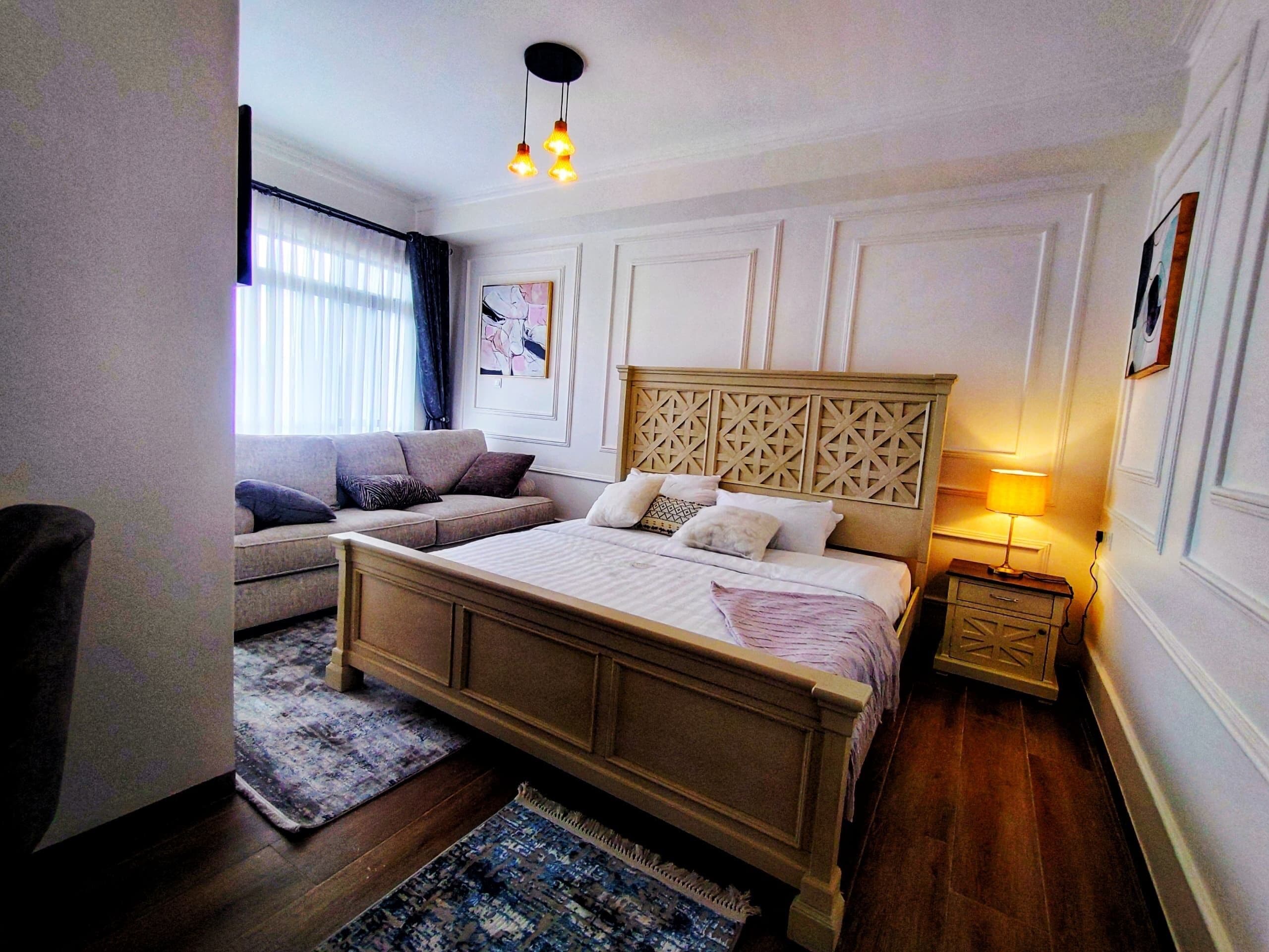 A bedroom with a bed, a sofa, a nightstand, a lamp, and a window with curtains.