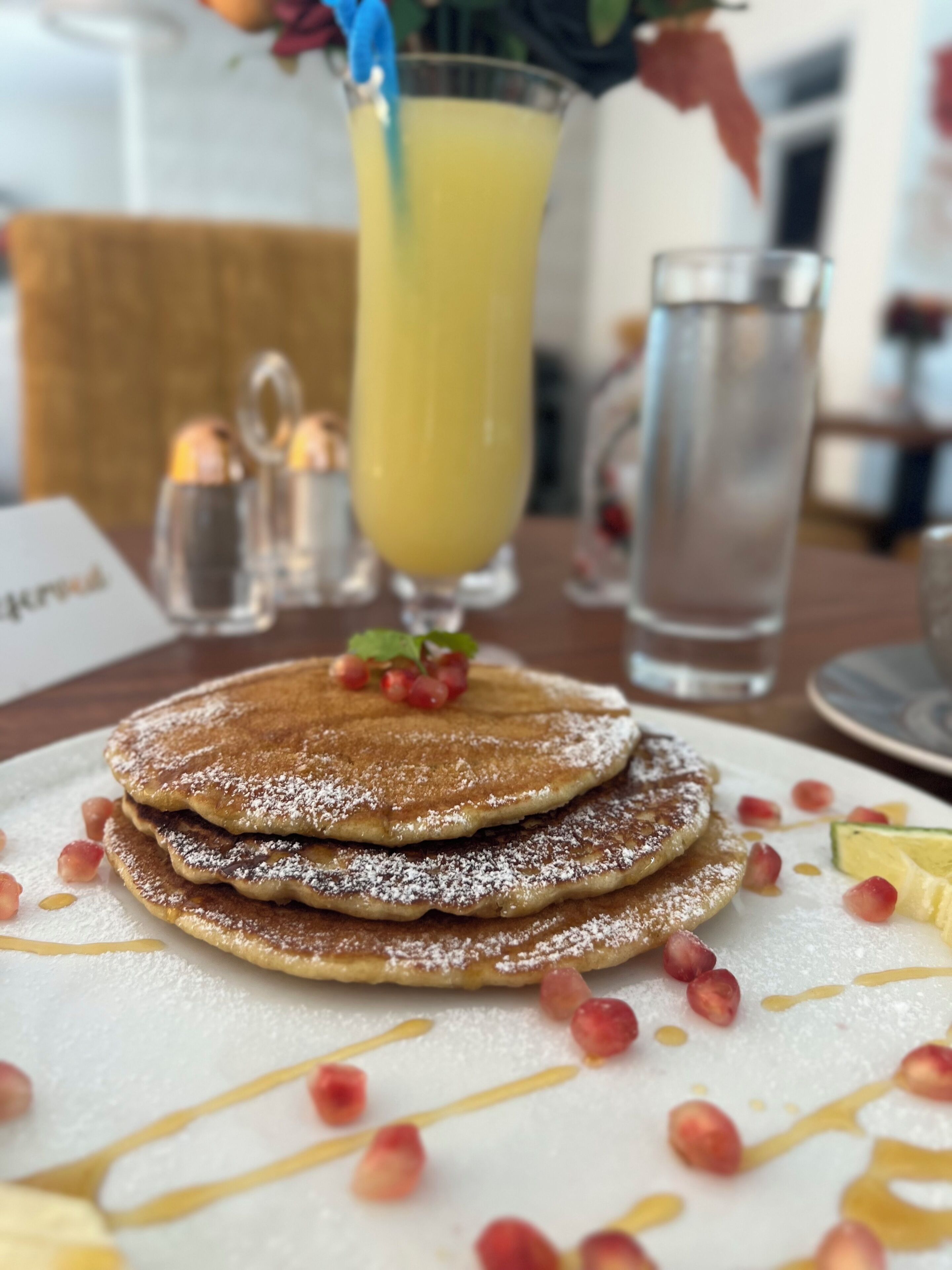 A stack of pancakes with syrup and powdered sugar, garnished with berries, on a white plate.