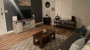 Ein Wohnzimmer mit Fernseher, Couchtisch, Sofa und einem Fenster mit Jalousien.