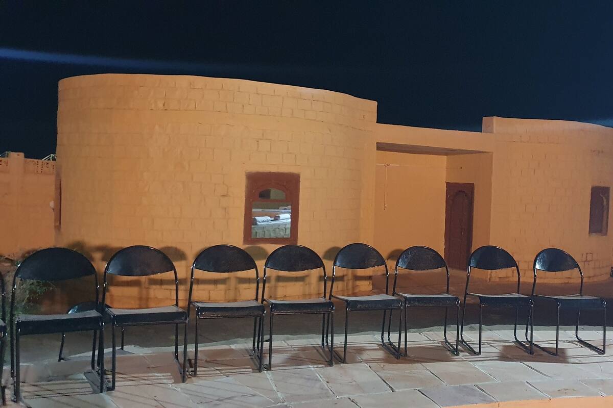 A row of black metal chairs aligned against a beige brick wall with a window.