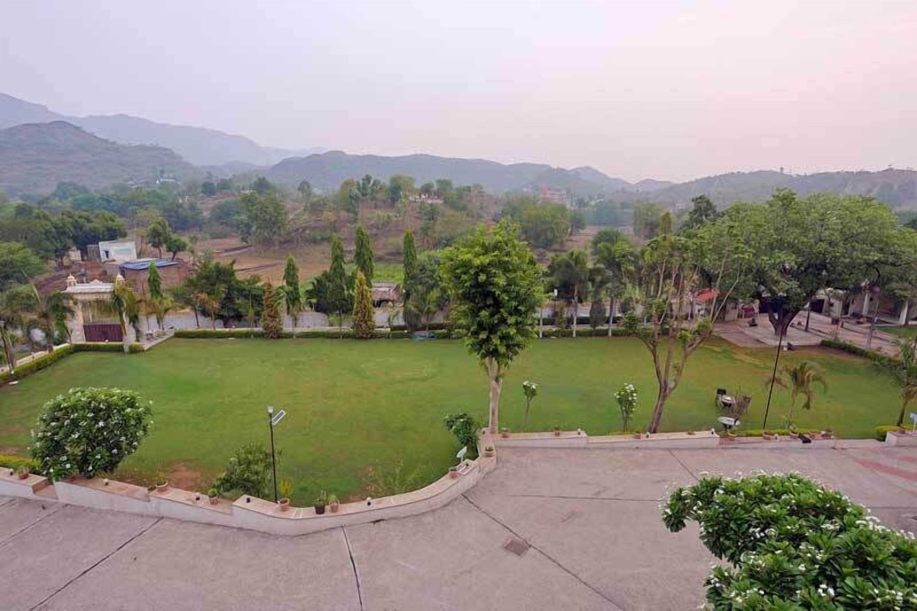 A view of a landscaped area with a large open grassy field, surrounded by trees and a few buildings in the background.