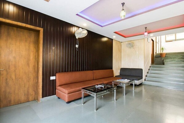 A modern lobby with a brown leather sofa, a glass coffee table, and a black armchair. There is a staircase with a potted plant on the landing. - Meera Valley Resort (Udaipur)