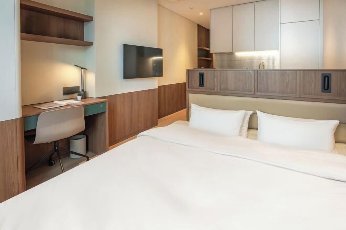 A hotel room with a bed, a desk, a chair, a TV, and built-in cabinets.