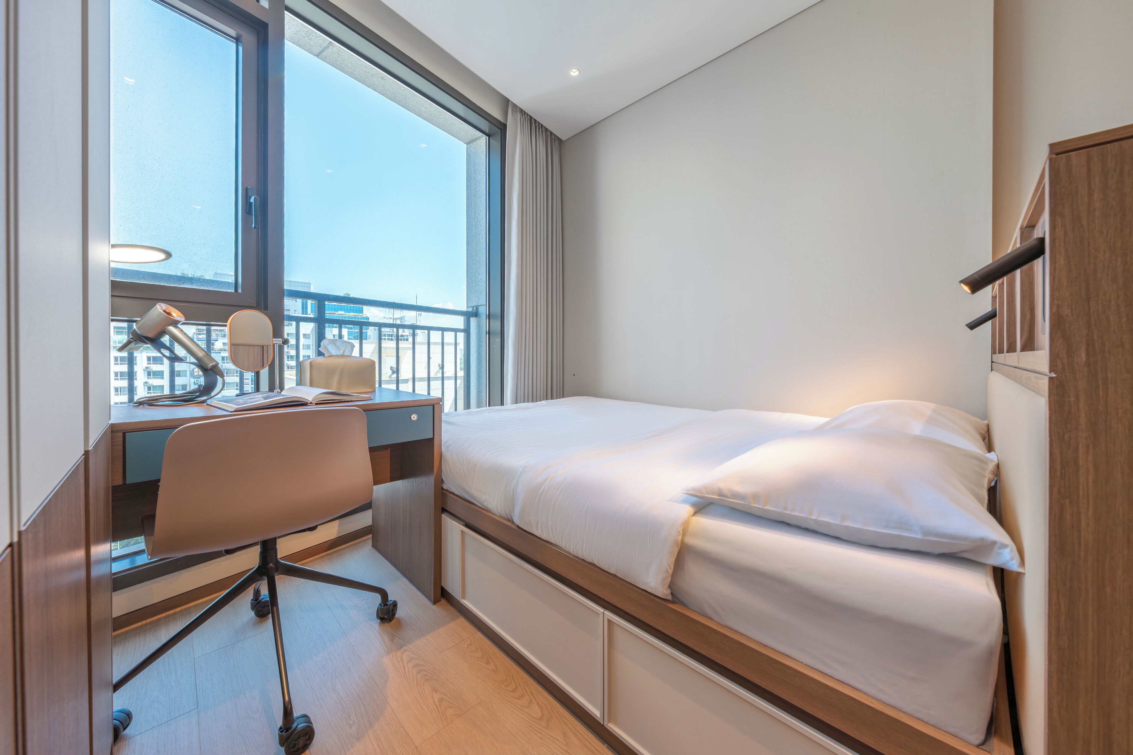 Habitación de hotel con cama, escritorio, silla y vistas a la ciudad a través de amplias ventanas.